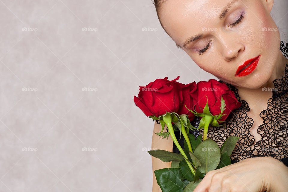 Beautiful woman between 30 and 35 years keeps red roses having closed eyes.