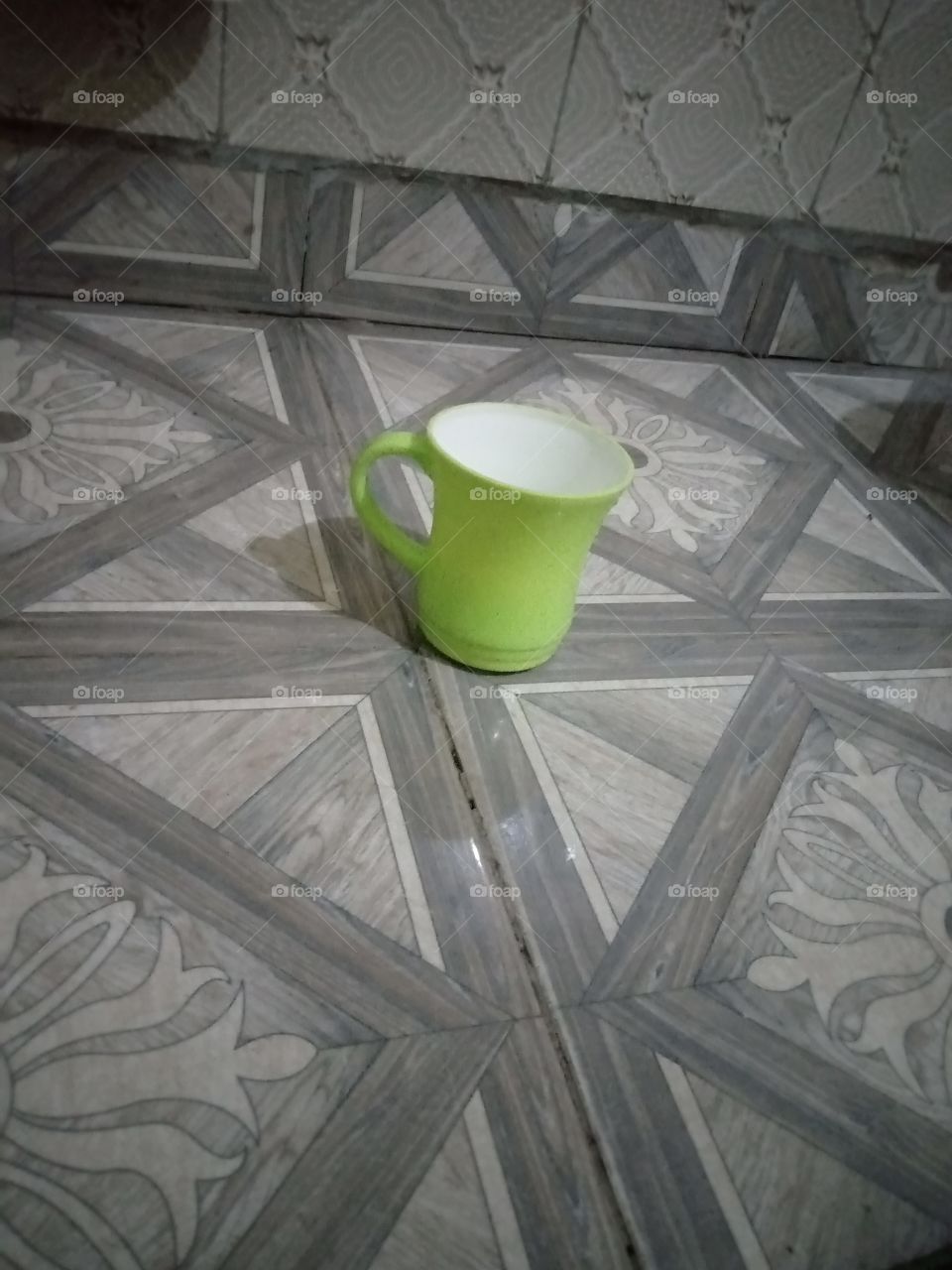 a cup on the floor casting down shadow back ward. it's a lemon green cup with a white colour inside.