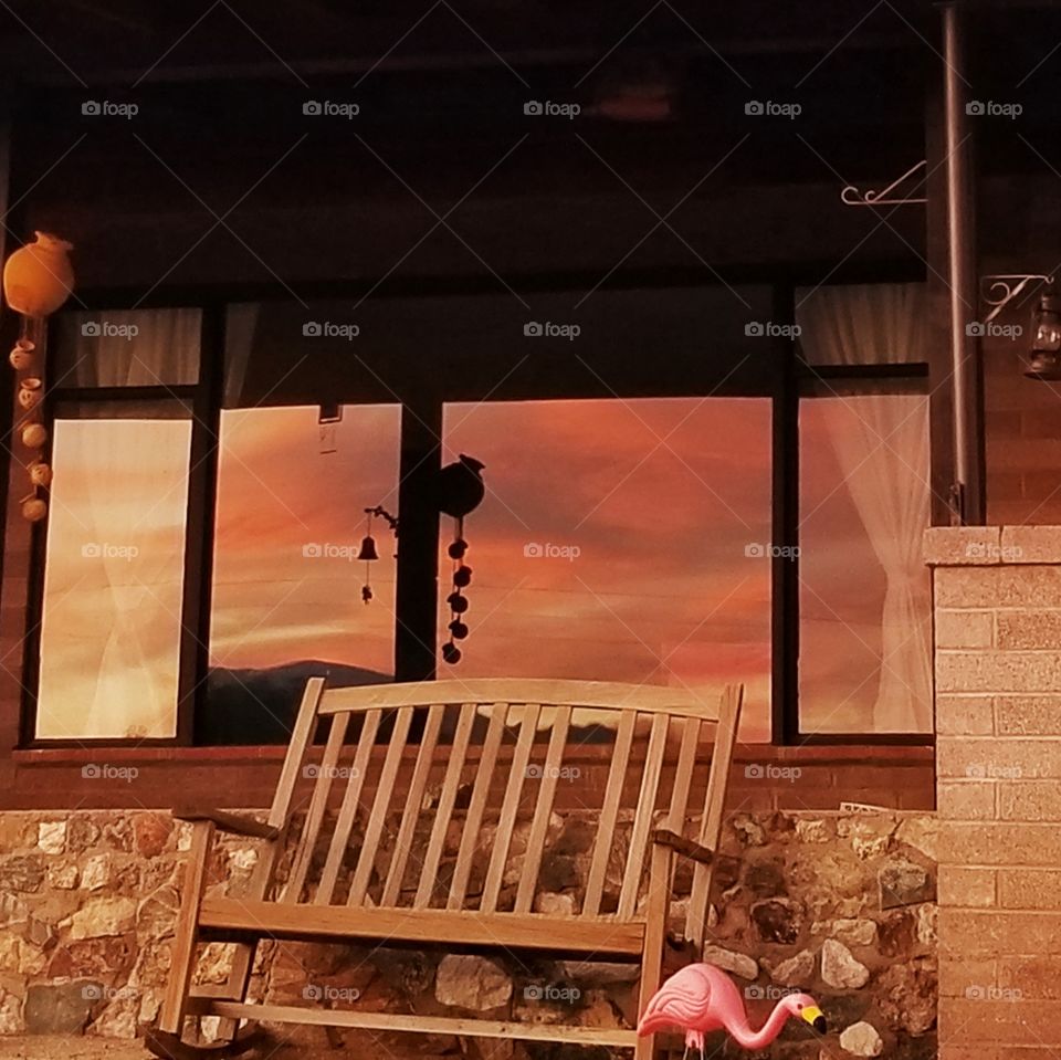 Sunset reflection in a large picture window. Rustic house at evening time.