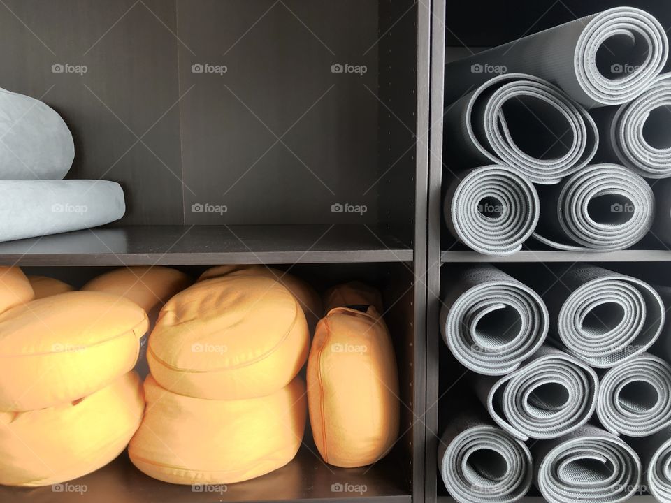 Grey yoga mats and orange yoga cushions in a black cupboard ready for the yoga class