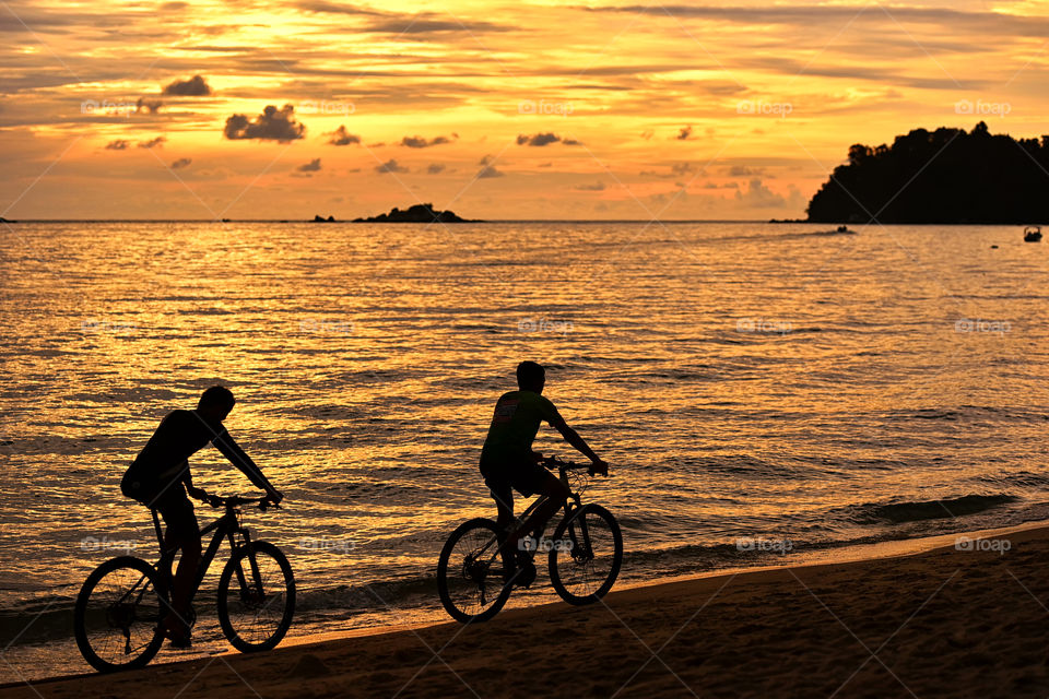 Two silhouette man ride a bike during sunset on the beach