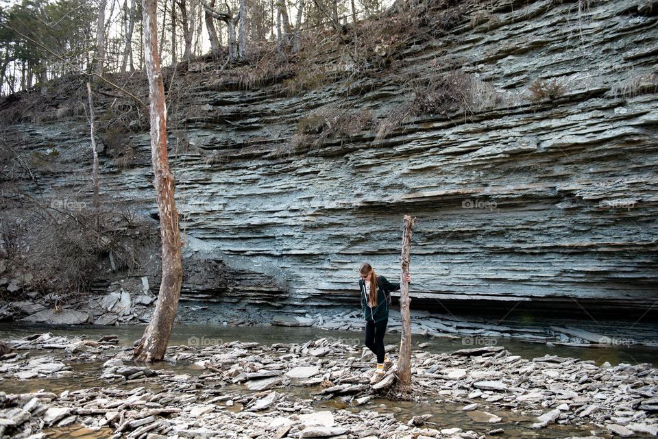 Woman hiking along a creek with a rock wall at Caesar’s Creek state park 