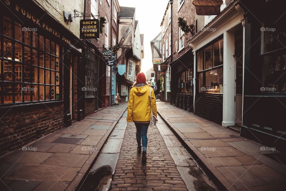 A rear view of a fashionable young girl wearing a bright yellow coat walking down the shambles mediaeval street in York UK in a lifestyle image