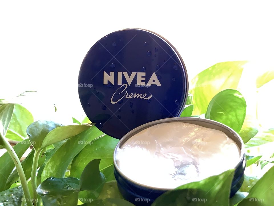 Nivea cream opened and used sat on the green leaves. Blue and white, beauty products.