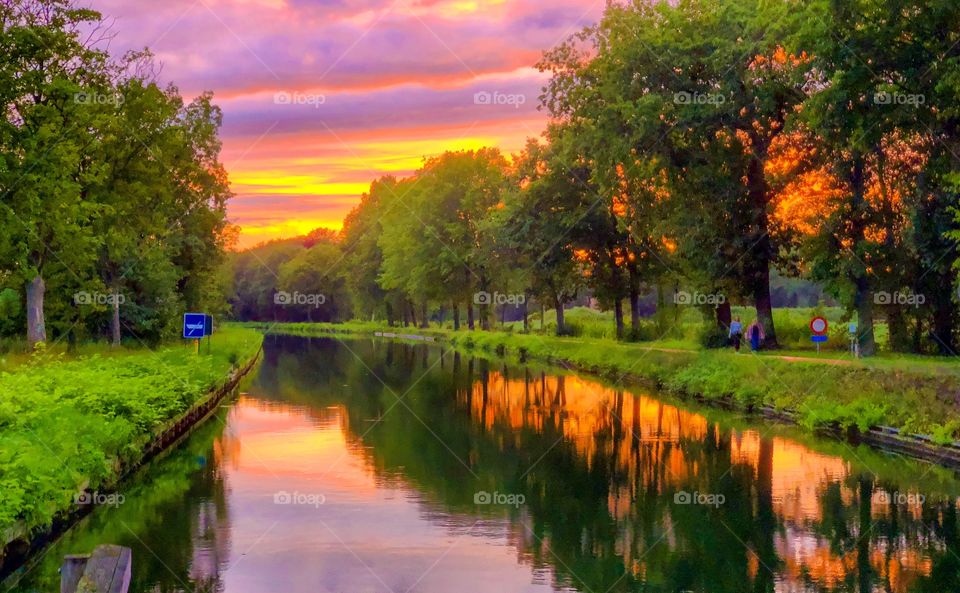 Dramatic colorful sunset sky reflected in the water of the river running through a green natural Countryside area