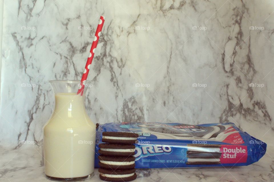 Oreo double stuff cookies stack next to a carafe of milk with a red and white straw on a marble backdrop