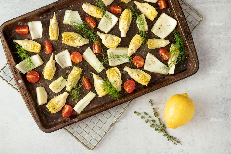 Flat lay of freshly cut artichoke, fennel and tomato on a sheet pan