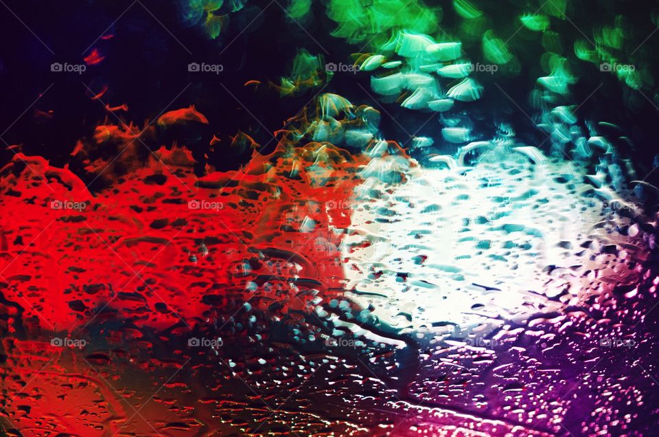colorful lights blurred on a pane of glass covered with water drops abstract colors