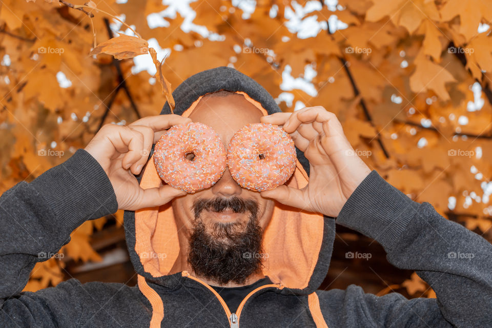 Funny portrait of man with donuts at autumnal background.