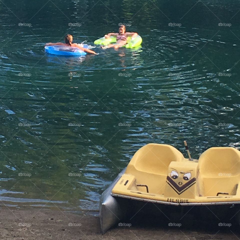 Two girls floating in pond, paddle boat