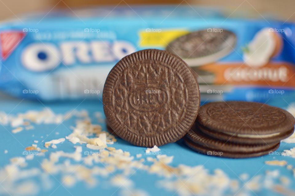 A stack of coconut Oreo thin cookies on a blue background with coconut shreds