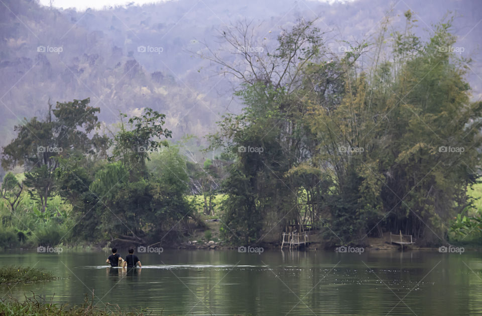 Man holding fishing nets walking in water Background blurred mountains and trees