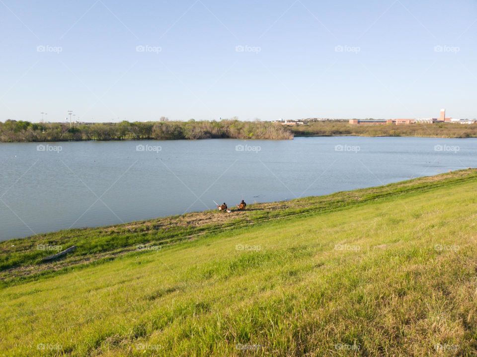 Two people fishing at a city park pond while sitting and relaxing.