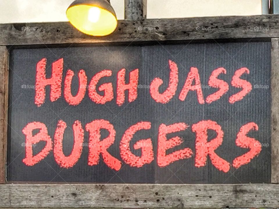 Eye catching outdoor wooden sign advertising burgers for sale with a clever twist of words.
