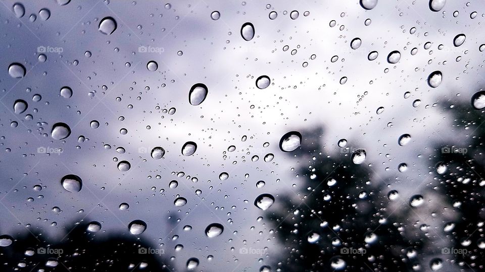 Raindrops on windshield of car after bad storm with sky in background.