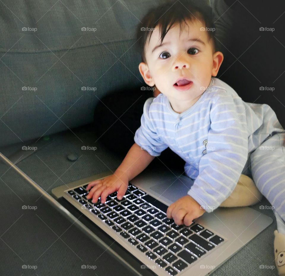 Close-up of a toddler sitting on sofa with laptop
