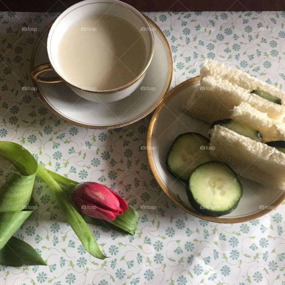 A fresh cucumber sandwich on white bread served with cucumber slices on a plate, displayed on a floral background with a tea cup and a pink tulip. USA, America