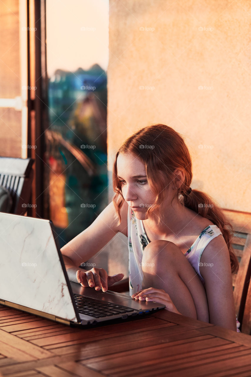 Woman working at home, using portable computer, sitting on patio on summer day. Candid people, real moments, authentic situations