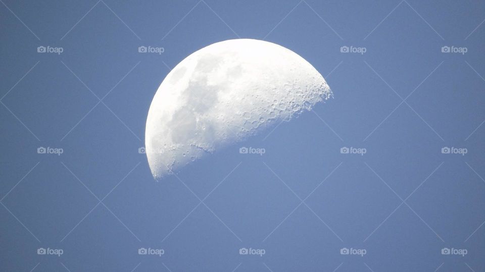 Very rate closeup of half moon on a baby blue pastel colored daytime sky