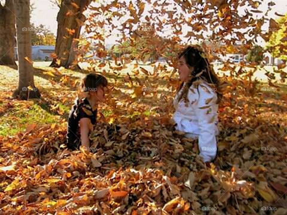 kids in leaf pile throwing leaves in the air in fall