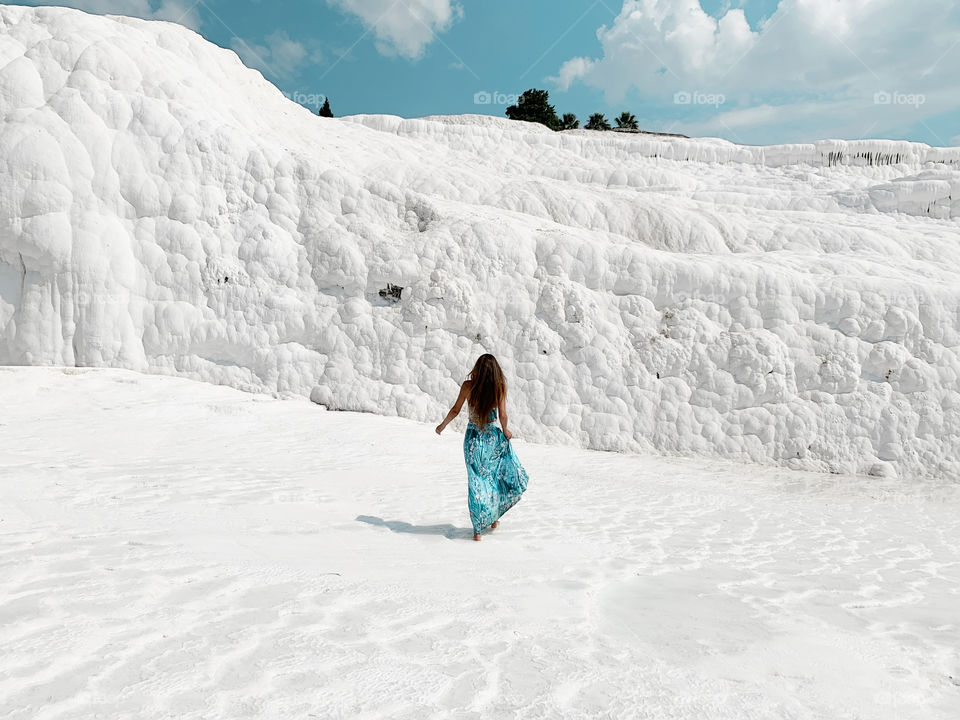 Young woman with long hair in blue dress walking by white chalk mountain 