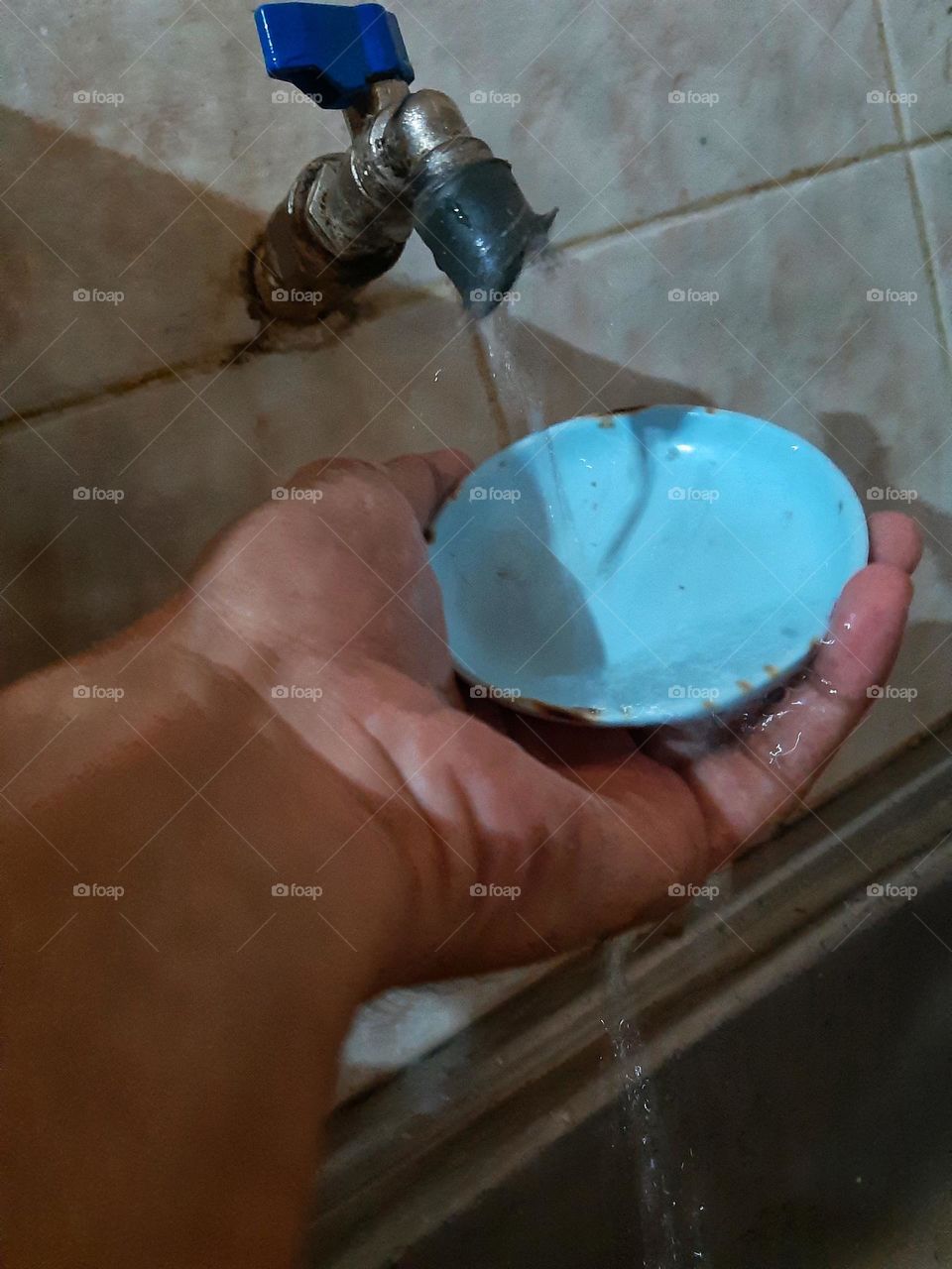 A colorful photo of a mini blue plate washed by a hand under a water tap