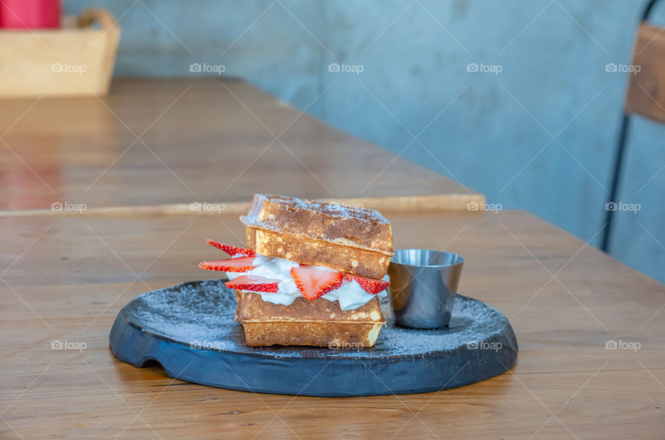 Waffle Strawerry fresh cream in the black plate on wooden table.