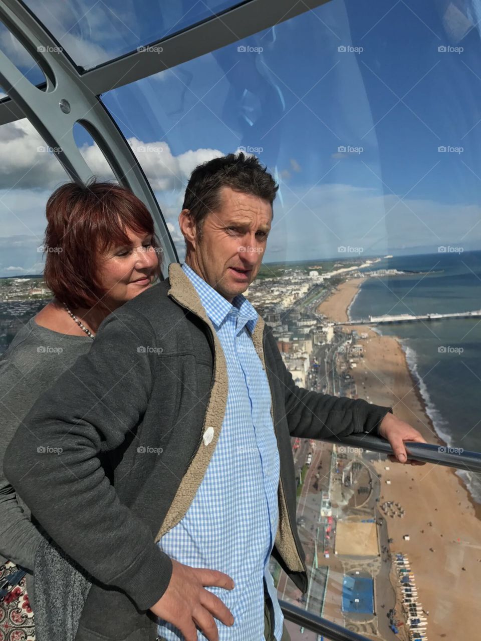 Couple are looking out over a stunning view of Brighton , beaches and sea. Beautiful day. At the highest point on i360 ride.