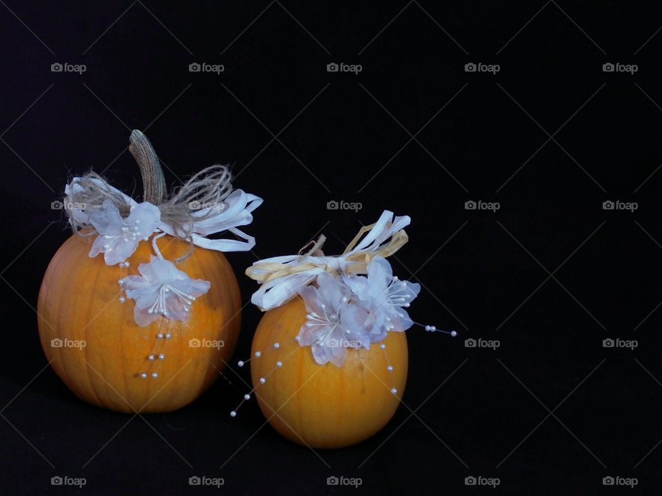 Two country style hand decorated pumpkins with beautiful white flowers and beads and brown and white paper lace against a black background with ample copy space. 