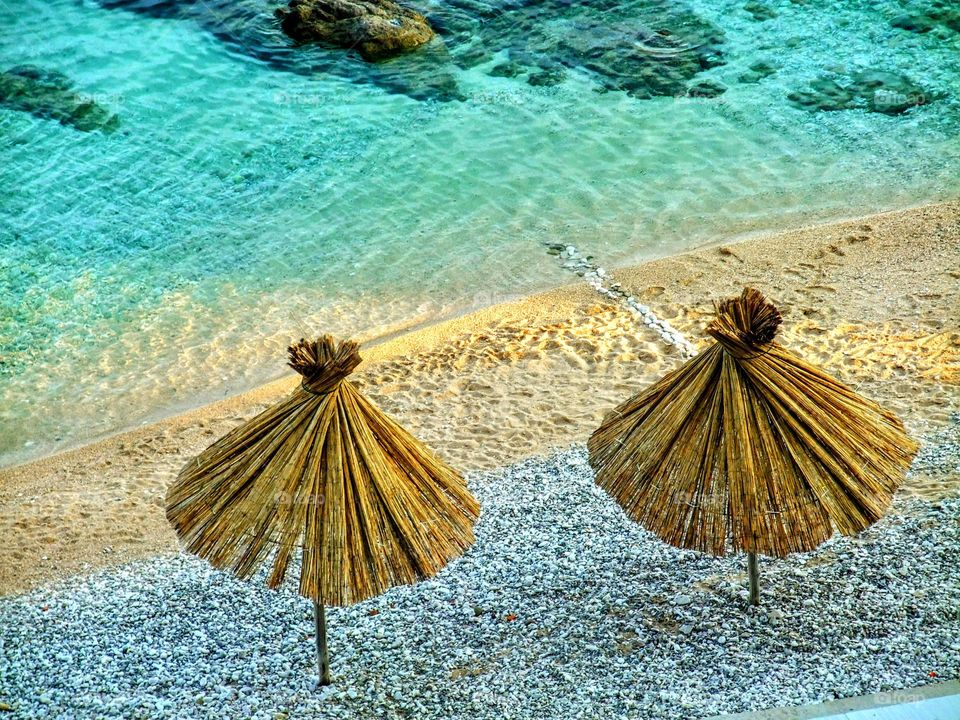 Golden straw sun umbrellas against white pebbles with a strip of golden sand and turquoise sea