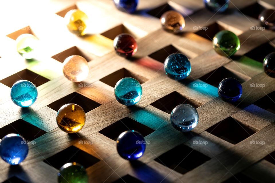 A portrait of a lot of colored glass marbles, which the light shining through them casts colorful shadows on the wooden surface.