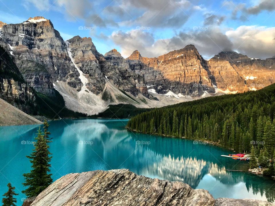 Mountains see the morning sun as the amazing glacial blue waters of Moraine Lake reflect them below