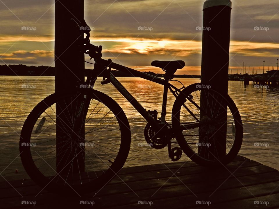 Cycling Week: Do you love your bicycle? A silhouette of a bicycle leans on the dock posts during a radiant sunset 