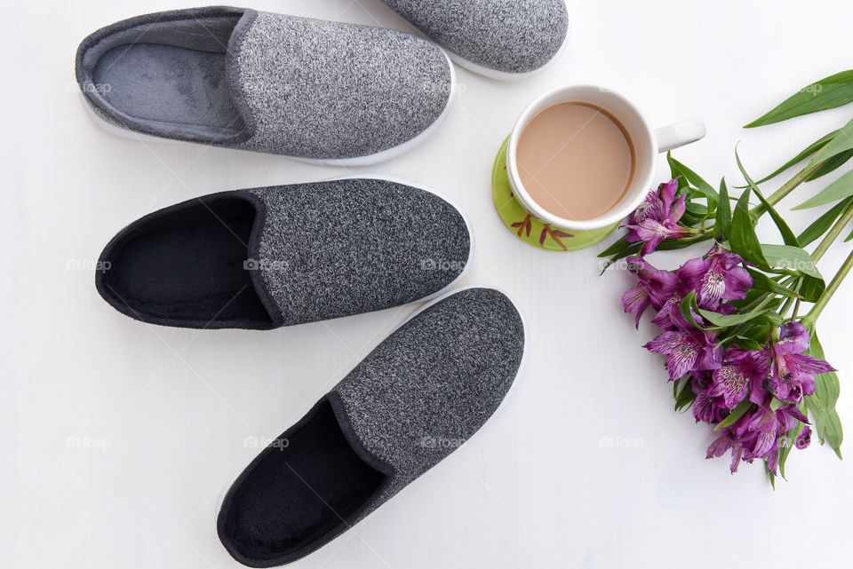 Flat lay of a cup of coffee next to slippers and bouquet of flowers