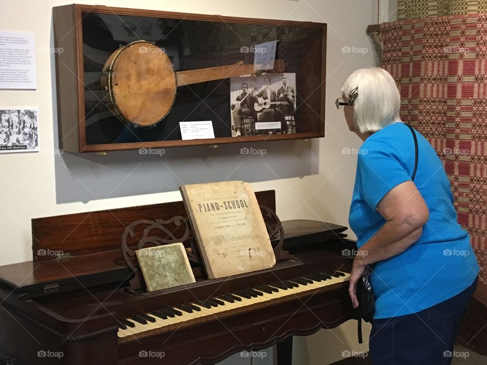Old piano and banjo on the wall. Woman looking at a old picture on the case of the man