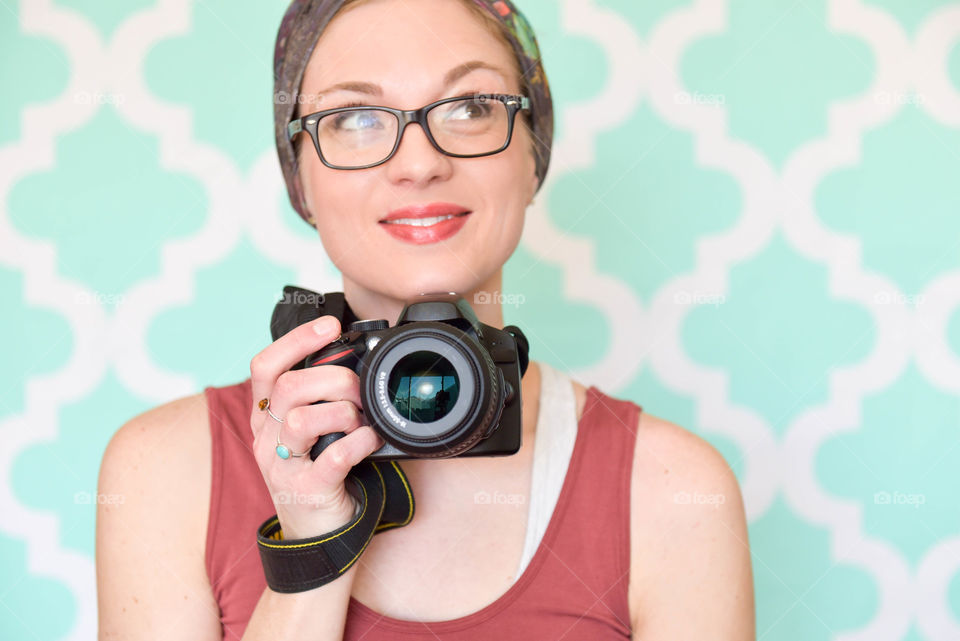 Young woman holding a digital camera and smiling indoors