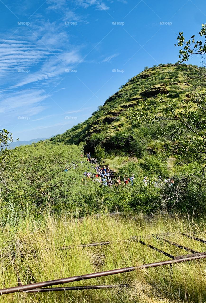 View of pilgrims going down the mountain on a pilgrimage walk of prayers. Mountains, bushes, trees, grasses and a railway metal. 