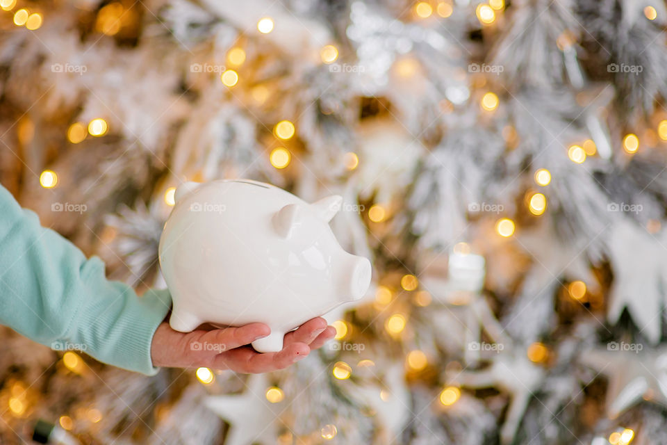 piggy bank with 100 dollars banknote in festive New Year atmosphere of scenery. Magical bokeh with Christmas tree and bright lights.