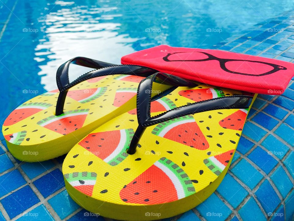 Flip flops with watermelons,pink sunglasses case near the pool