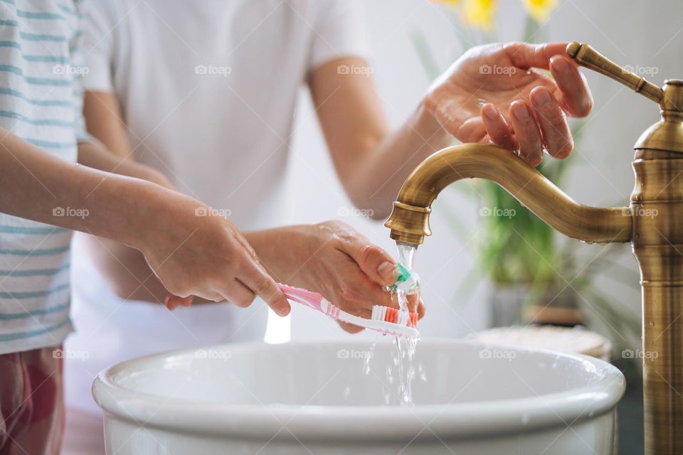 Young mother woman with long hair with little tween girl daughter in pajamas brushing their teeth in the morning at home