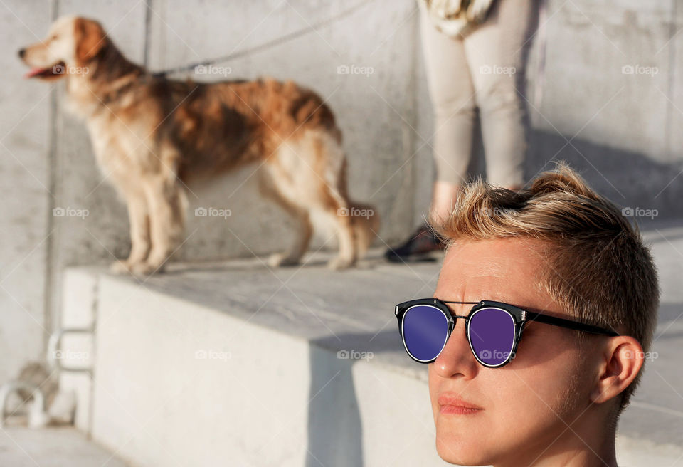 A woman portrait with modern colored sunglassess and a dog on the background