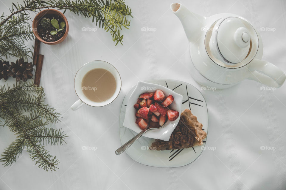 Tea, strawberries and pecan pie beside a teapot in a festive flat lay.