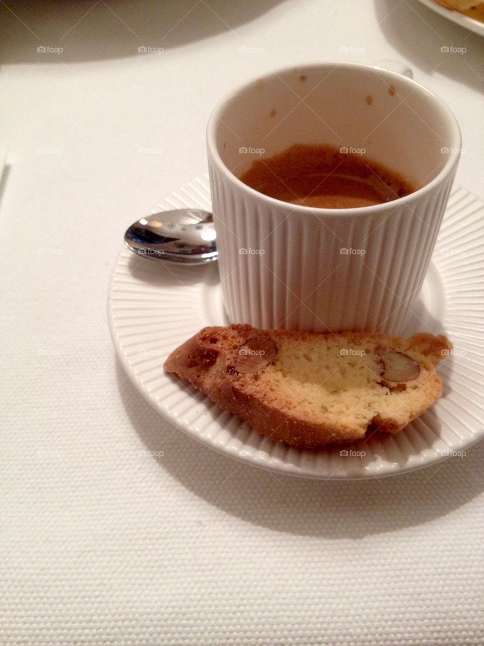 White espresso cup with a spoon and a cookie on a white tablecloth 