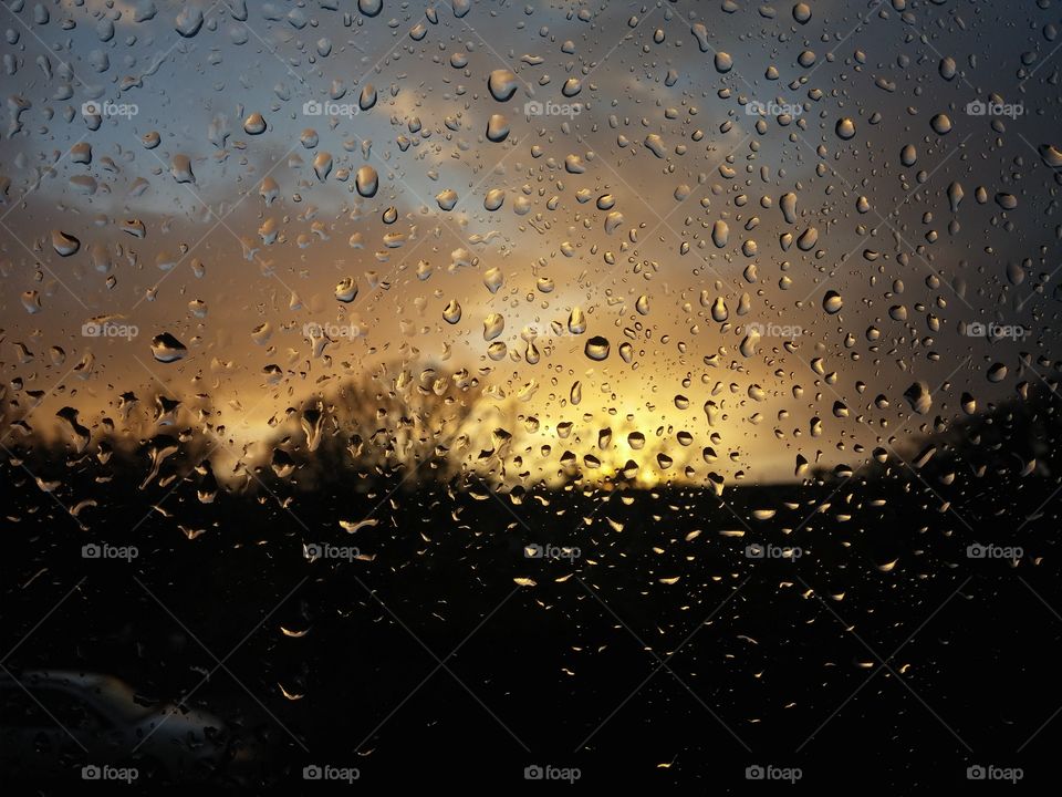 rain droplets on window with sunset in the background