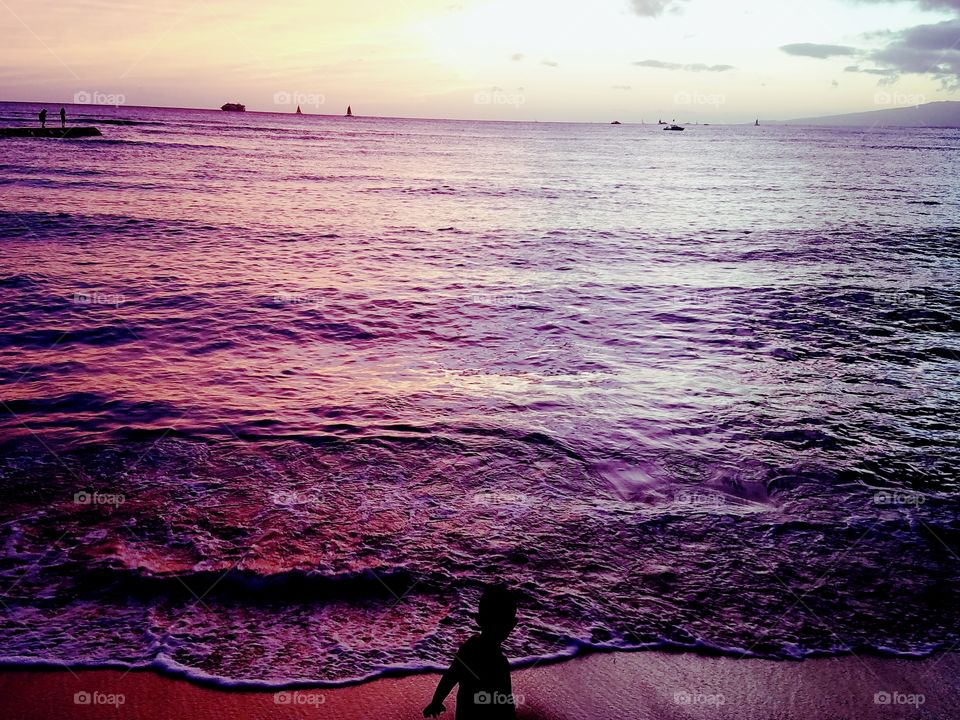 boy plays in the surf line painted purple and pink by the Waikiki Sunset