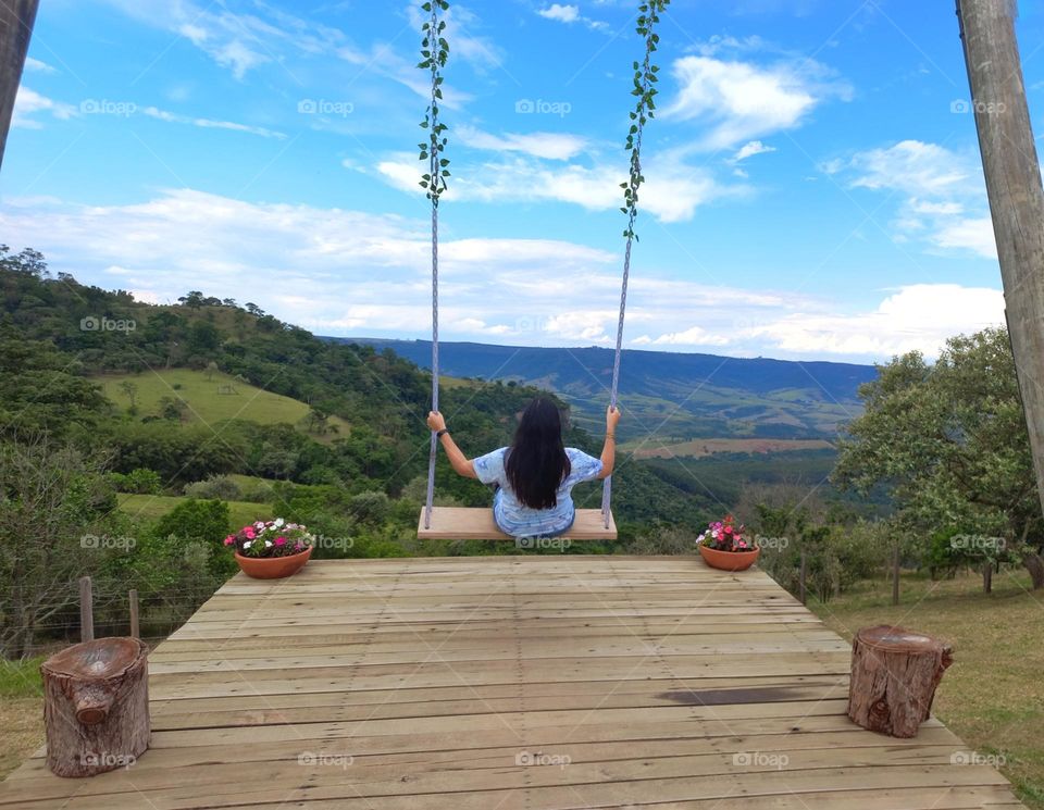 Girl on the swing seeing the atlantic forest, mountains and a blue sky