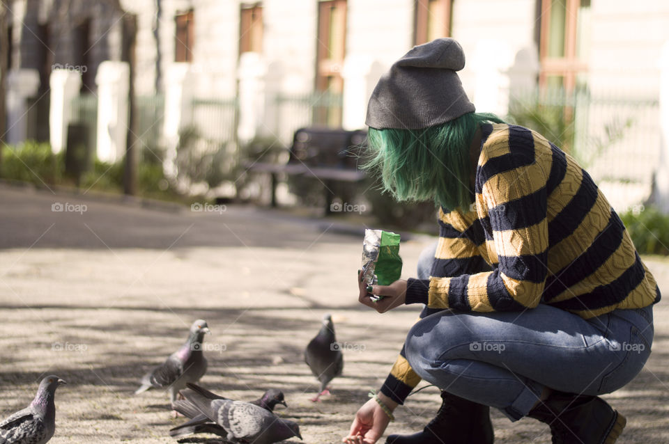 Alternative girl with green hair feeding animals in the park
