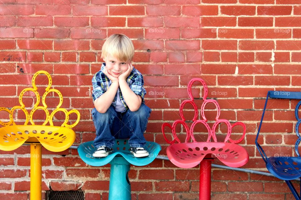 Boy sitting on chair against brick wall