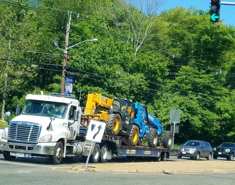Open bed truck hauling two tractors at intersection.