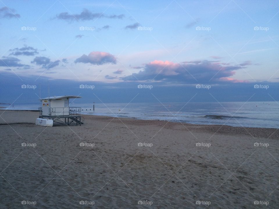 A pastel sunset at Bournemouth beach with lifeguard hut and blue and pink hues. A calm beach. Sand and water. By the sea. Seashore. 